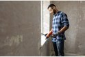 Man met veiligheidsbril, een blauw geruit shirt en handschoenen gebruikt een oranje Black+Decker verfbrander bij een raam.