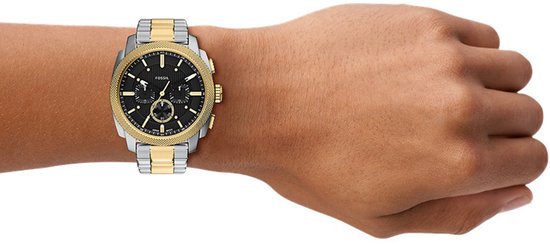 Gouden en zilverkleurig Fossil horloge om een pols met donkere huidskleur.