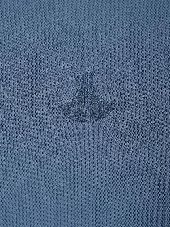 Detail van een geborduurd ankerlogo op een blauw poloshirt.