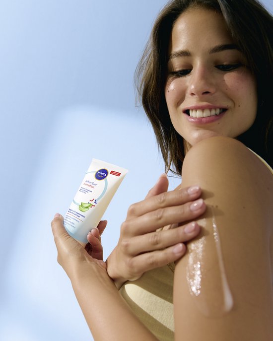 Vrouw met arm ingesmeerd met aftersun gel. Houdt de NIVEA SUN After Sun Sensitive tube vast. Zachte glimlach, lichte achtergrond.