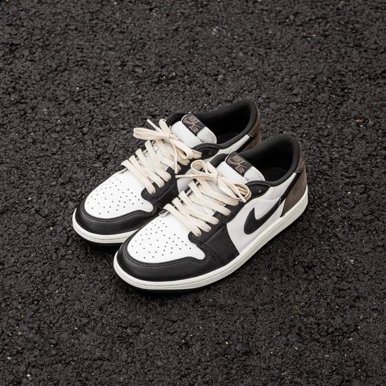 Een paar lage zwarte en witte sneakers met gebroken witte veters, liggend op asfalt.