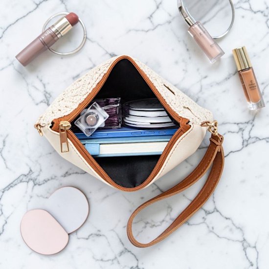 Open crèmekleurig gehaakt tasje met bruine leren polsband, gevuld met cosmetica en een notitieboekje.