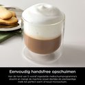 Glazen mok met warme chocolademelk en een dikke laag melkschuim, naast koekjes.