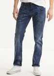 Man draagt een blauwe spijkerbroek met stonewash-effect en opgerolde pijpen. Witte sneakers.