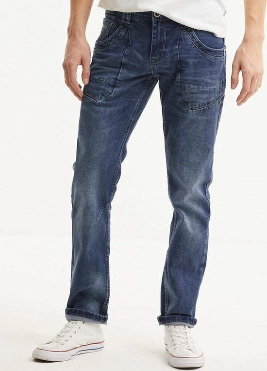 Man draagt een blauwe spijkerbroek met stonewash-effect en opgerolde pijpen. Witte sneakers.