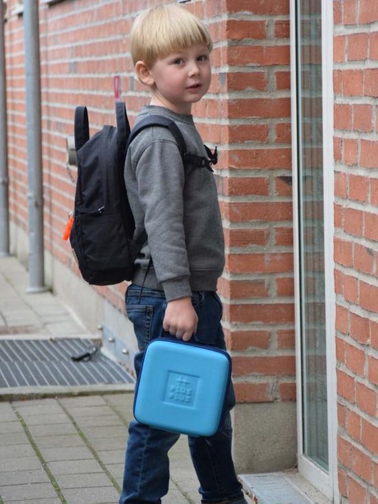 Een jongen met een rugzak en een turquoise Plus-Plus koffer in zijn hand, staand bij een deur.