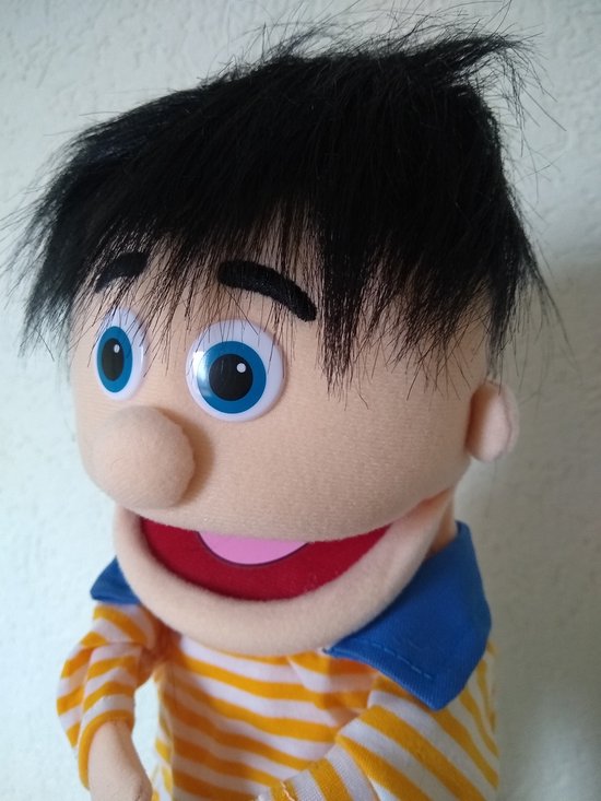 Detailopname van handpop Bobbie met zwart pluizig haar, blauwe ogen, en een gele-oranje gestreepte trui met blauwe kraag.