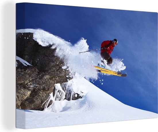 Canvas Schilderij Een skiër maakt een jump vanaf een besneeuwde rots - 90x60 cm - Wanddecoratie