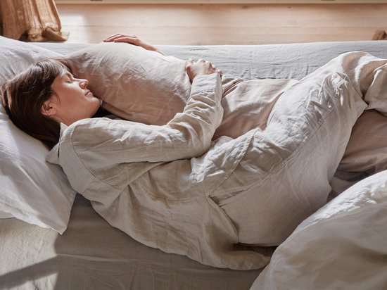 Une femme dort dans un lit, serrant un long traversin en satin taupe.