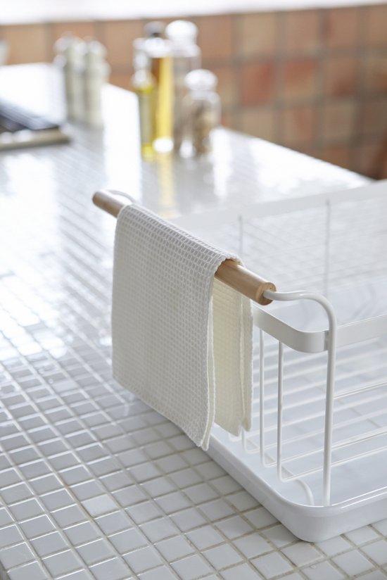 Détail d'une serviette blanche suspendue à la poignée en bois d'un égouttoir blanc.
