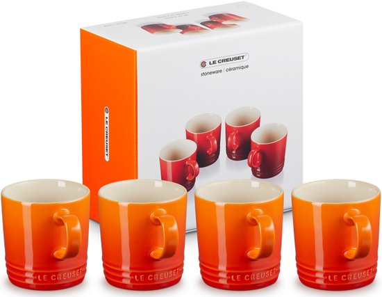 Quatre mugs Le Creuset orange devant une boîte de quatre mugs Le Creuset rouges.