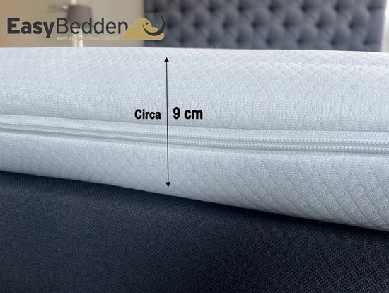 Witte topper met ruitpatroon, dikte van circa 9 cm. Geplaatst op een bed met donkergrijze hoofdbord.