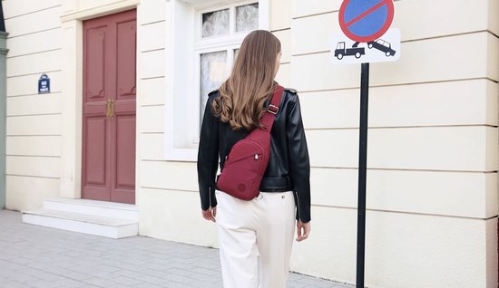 Een vrouw met lang bruin haar draagt een bordeauxrode crossbodytas over een zwart leren jack.