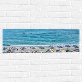 WallClassics - Muursticker - Rieten Parasols met Ligbedjes op het Strand - 90x30 cm Foto op Muursticker