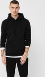 Man met kort bruin haar draagt een zwarte hoodie over een wit T-shirt, met spijkerbroek.