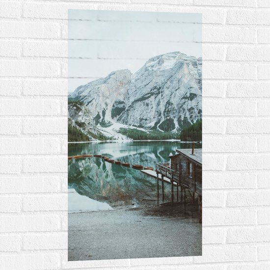 WallClassics - Muursticker - Houten Huisje met Bootjes in Sneeuwgebied - 50x100 cm Foto op Muursticker