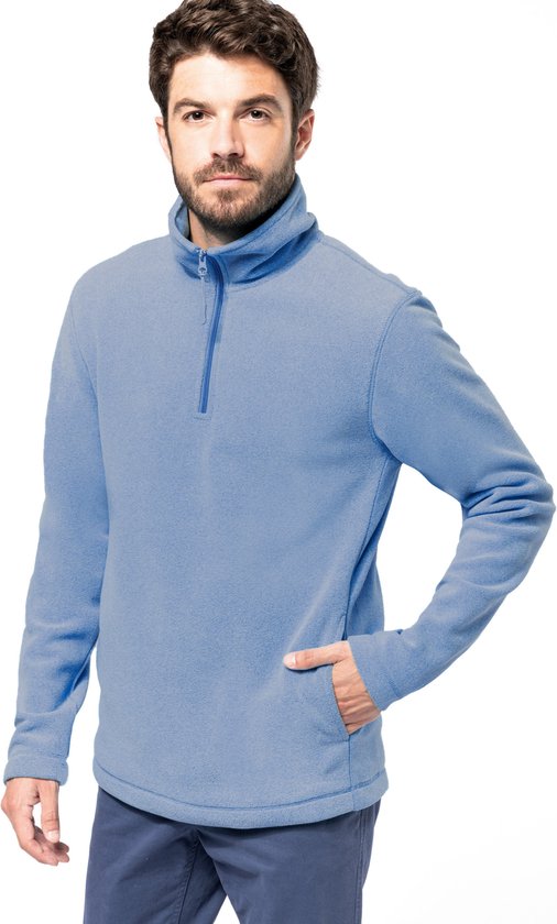 Homme avec la main dans la poche de son pull bleu à demi-zip et col haut.