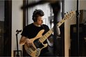 Jonge man met zwarte koptelefoon speelt basgitaar in een studio.