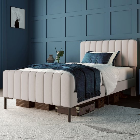 Un lit rembourré beige clair avec une couverture et des coussins bleu foncé, dans une chambre avec des panneaux muraux bleus.