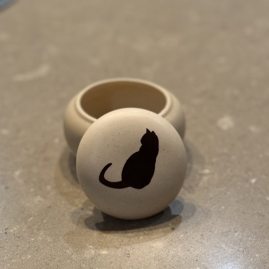 Licht beige zandstenen mini-urn met het deksel ernaast. Het deksel heeft een bruine, gestileerde zittende kat.