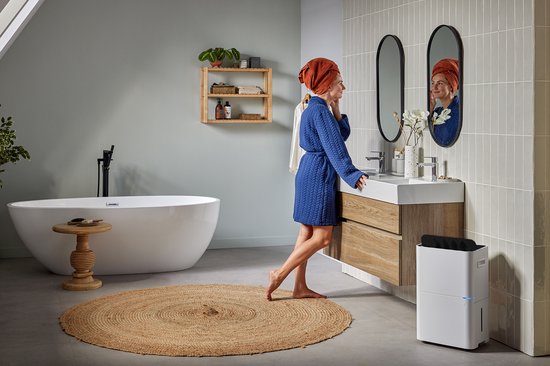 Witte Qlima luchtontvochtiger op de vloer in een moderne badkamer naast een wastafelmeubel.