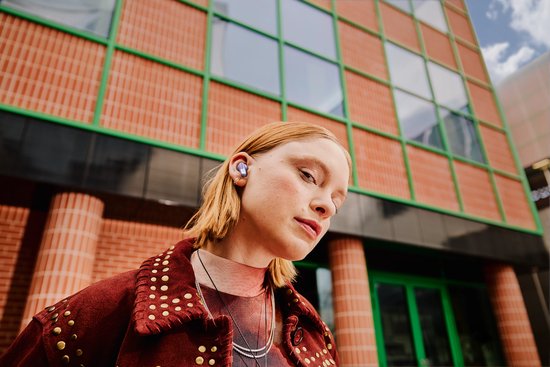 Model met een paars oortje in haar oor, met een gedurfde jas met studs.