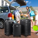 Familie die bagage in een auto laadt, met drie zwarte koffers van TAN.TOMI op de oprit.