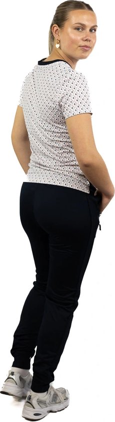 Model draagt een donkerblauwe sportbroek en een wit T-shirt met zwarte stippen, met de handen in de zakken.