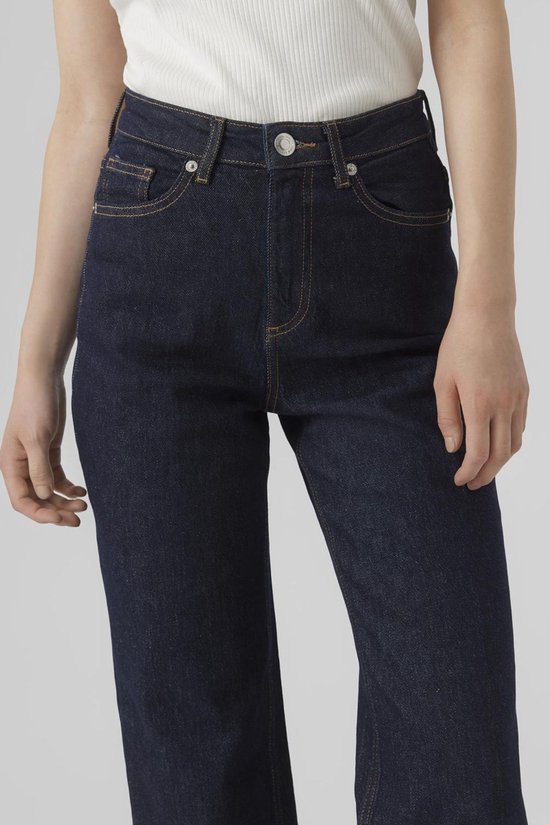 Close-up van model in donkerblauwe wijde jeans, witte top en sneakers.