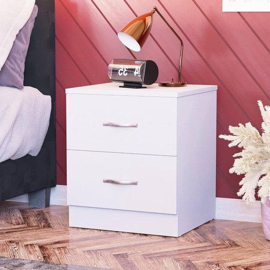 Wit nachtkastje met twee lades en zilverkleurige handgrepen, naast een bed.