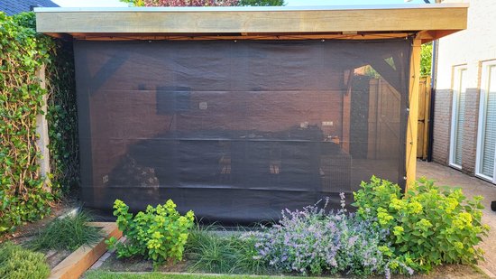 Zwart verandadoek van 300x225 cm, opgehangen aan een houten overkapping met groen en paars groen in de tuin.