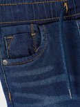 Detail van donkerblauwe spijkerbroek met stonewashed effect. Oranje stiksels, trekkoord en knoop aan de voorzijde.