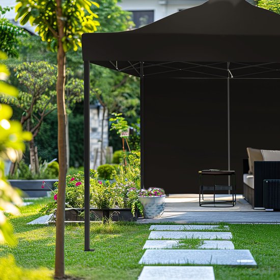 Zwarte partytent in een weelderige tuin, deels bedekt door een boom. Een deel van de tent is zichtbaar met meubilair eronder.