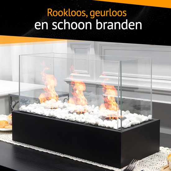 Een rechthoekige sfeerhaard met drie vlammen, witte stenen en een glazen omhuizing, op een tafel met servies. Tekst: Rookloos, geurloos en schoon branden
