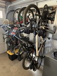 Meerdere fietsen hangen aan zwarte muurhaken in een garage, met een gele krat eronder.