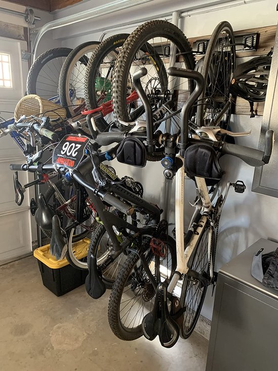Meerdere fietsen hangen aan zwarte muurhaken in een garage, met een gele krat eronder.