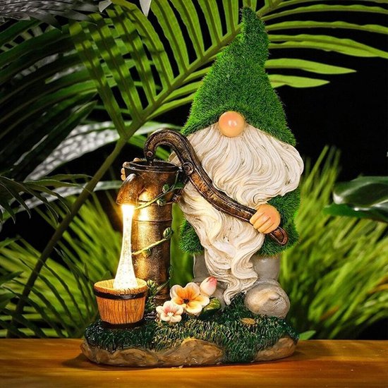 Gnome de jardin illuminé avec tenue verte, barbe blanche et pompe à eau, avec des plantes.