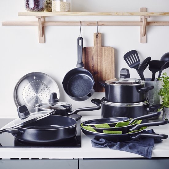 Un ensemble de poêles noires avec couvercles en verre et une passoire métallique sur un comptoir.