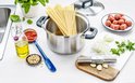 Een kookpan gevuld met spaghetti, omringd door ingrediënten op een aanrecht.