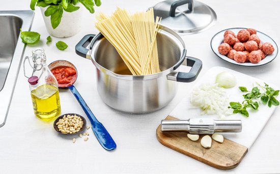 Een kookpan gevuld met spaghetti, omringd door ingrediënten op een aanrecht.