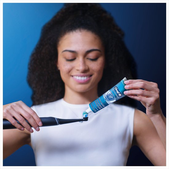 Vrouw met krullend haar brengt Oral-B tandpasta aan op elektrische tandenborstel.