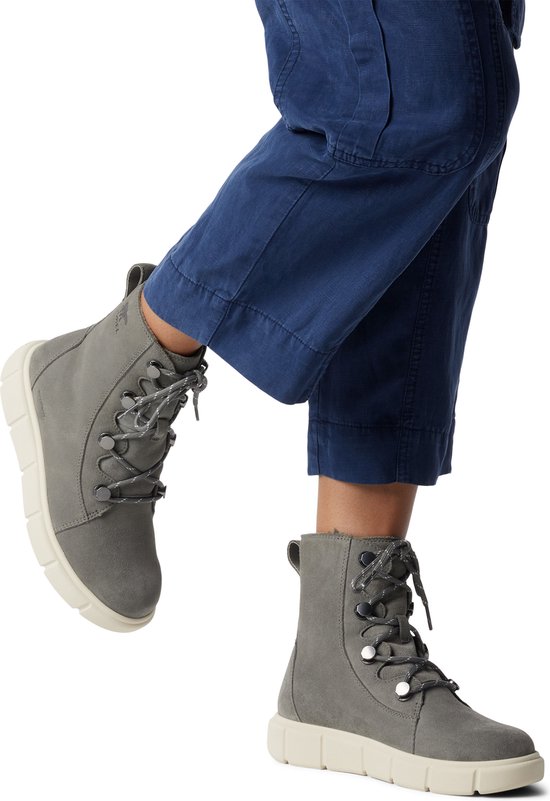 Voeten van een persoon die grijze Sorel laarzen met crème zolen en blauwe cargo-broek draagt.