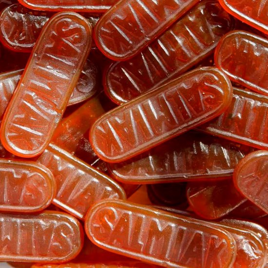 Een close-up van vele oranje-bruine, langwerpige dropjes met de tekst 'SALMIAK'.
