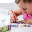 Une fille réalise un magnet Stitch diamond painting avec des perles violettes et bleues et un stylo rouge. Elle tient le magnet, d'autres magnets finis sont à côté.