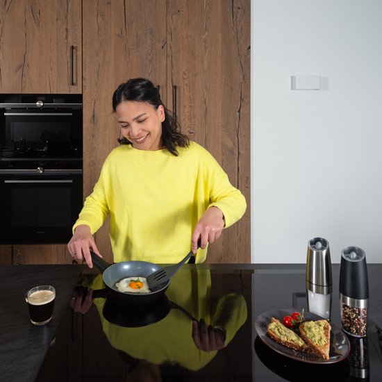 Een vrouw in een gele trui bakt een ei in een koekenpan in een keuken.