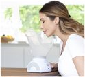 Vrouw met een witte top inhaleert stoom uit een Medisana gezichtssauna met brede, transparante kap.