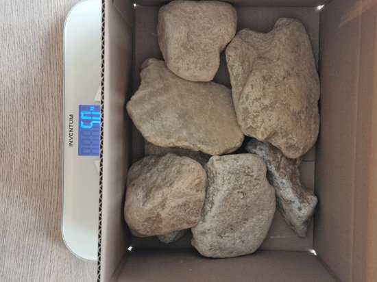 Vijf lichtbruine, onregelmatig gevormde spekstenen in een kartonnen doos op een weegschaal.