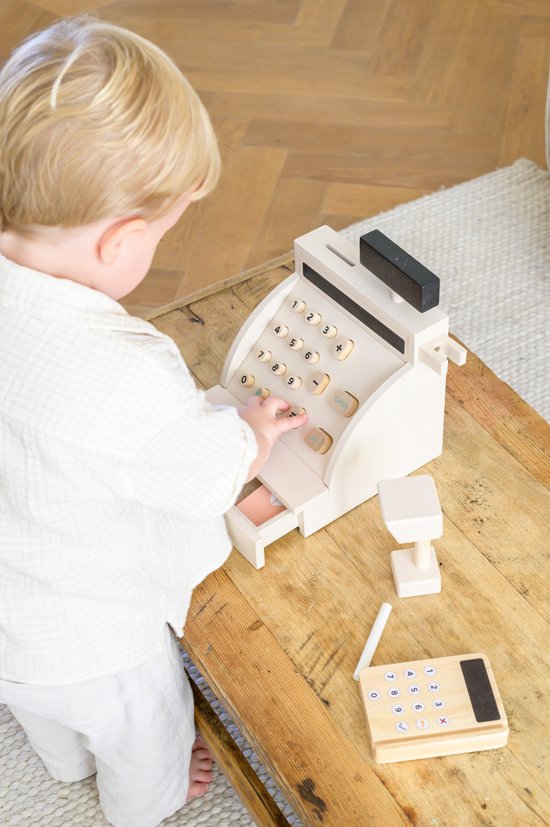 Kind speelt met een houten speelgoedkassa. Houten pinapparaat en losse tel-elementen ernaast.