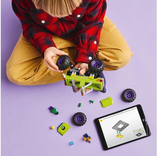 Jongen bouwt een groene LEGO monster truck met grote wielen en paarse velgen.