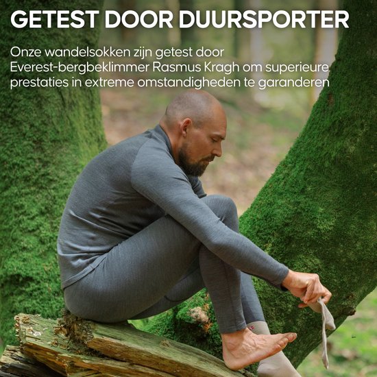Man in grijze thermokleding op een boomstronk, aantrekkelijk van de sokken, met tekst 'Getest door duursporter'